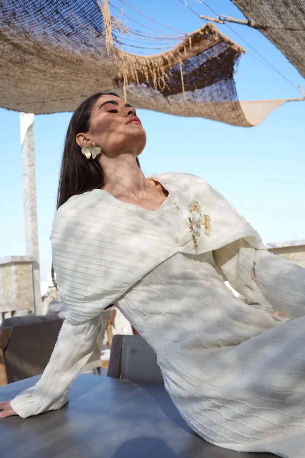 Detail of Ginkgo Bloom off-white dress showing textured fabric, cape collar, and gold pearl floral brooches.