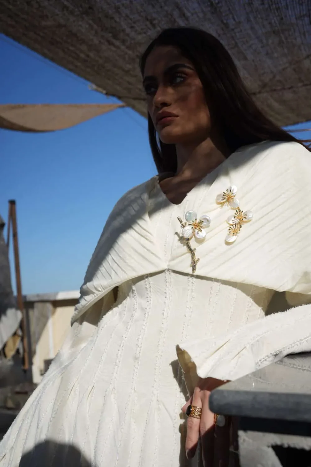 Model wearing Ginkgo Bloom off-white maxi dress sitting on a rooftop terrace in sunlight.
