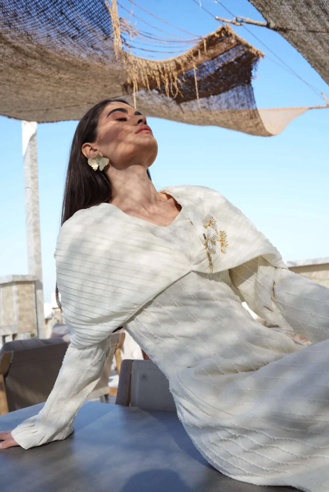 Detail of Ginkgo Bloom off-white dress showing textured fabric, cape collar, and gold pearl floral brooches.